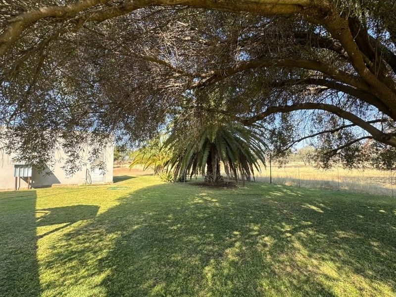 A spacious, well-maintained garden area featuring mature trees, expansive lawn, and clear views of the surrounding farm landscape.