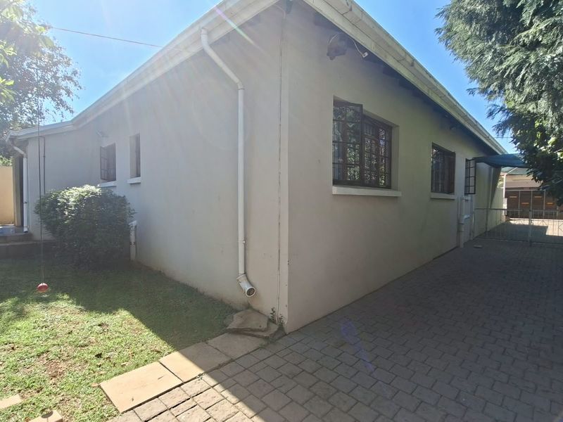 Rear exterior view of the property featuring a paved driveway, established garden area, and functional steel-framed windows.