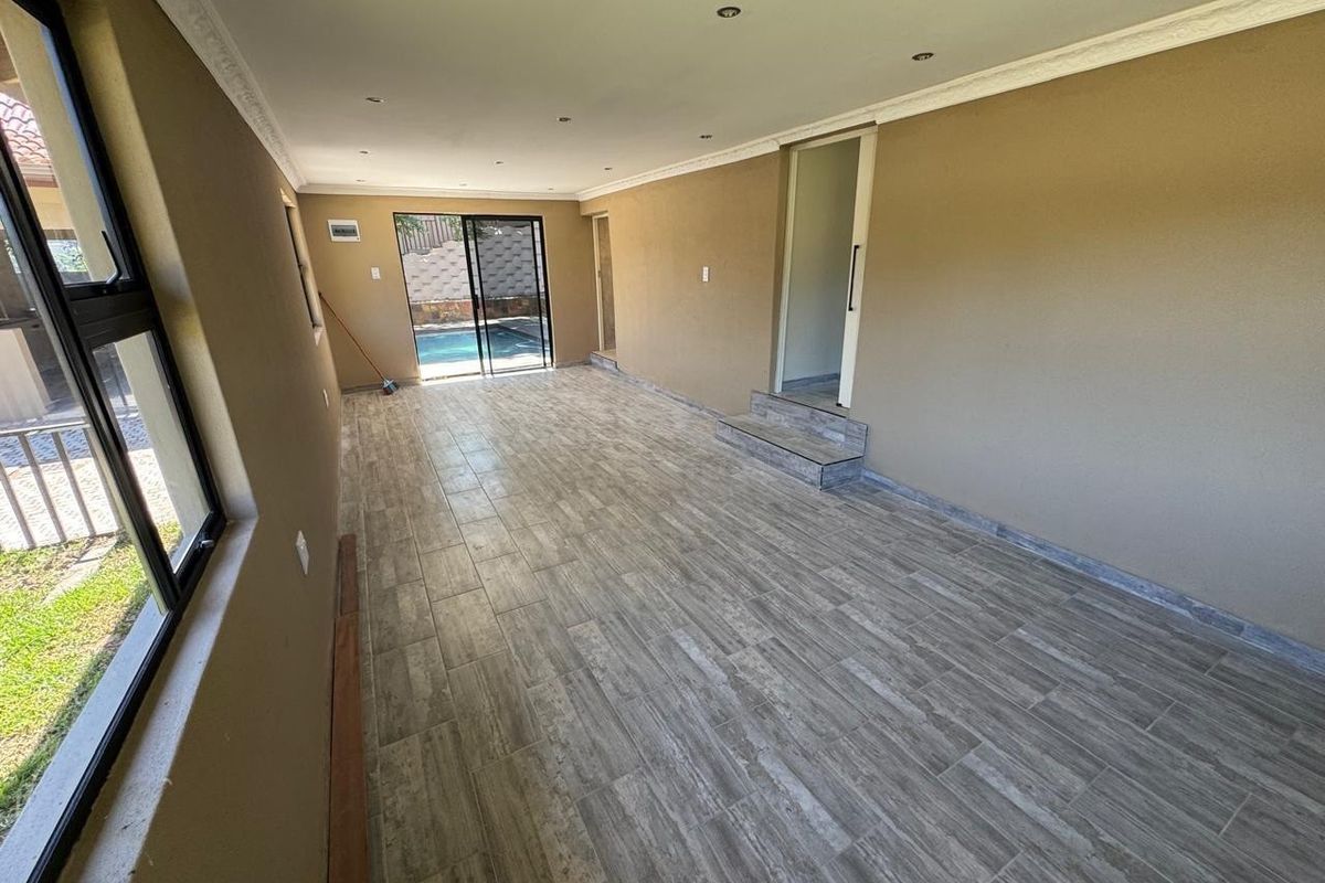 Spacious, empty living area featuring modern wood-look floor tiles, recessed lighting, and sliding glass doors providing direct access to the pool area.