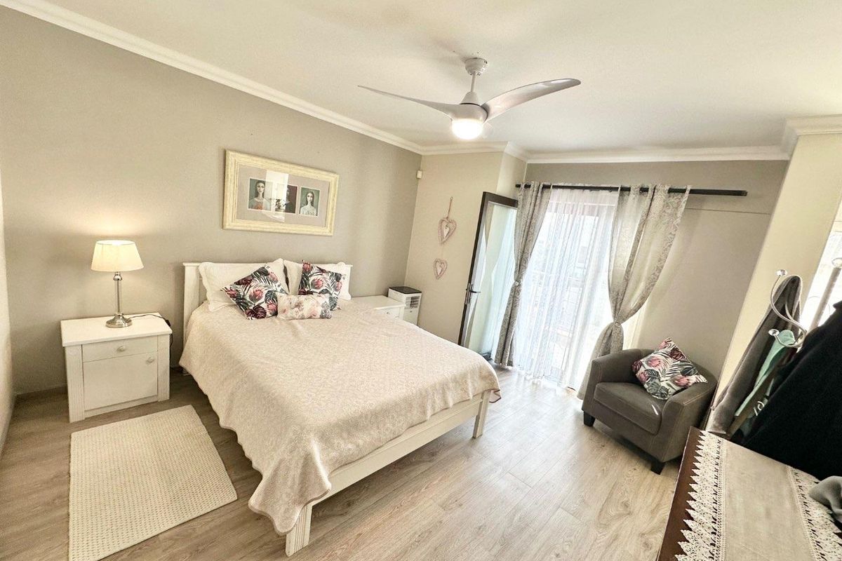 A well-maintained bedroom featuring light wood-look flooring, a ceiling fan, and a glass sliding door providing access to an outdoor balcony.