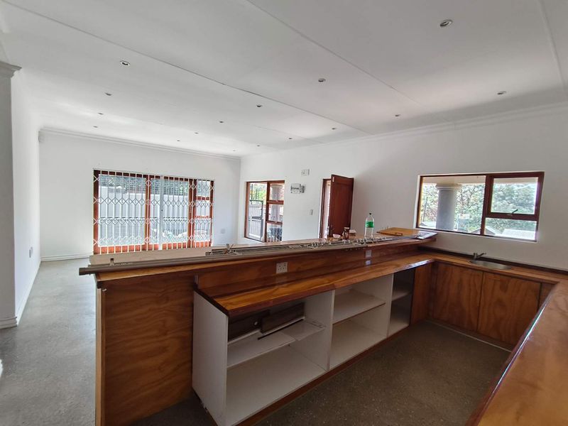 Spacious open-plan living and kitchen area featuring wooden cabinetry, a built-in breakfast bar, and large windows with security gates.
