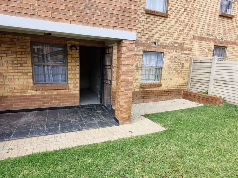 Rear exterior view of the apartment featuring a private tiled patio, paved walkway, and a small enclosed garden area with boundary walling.