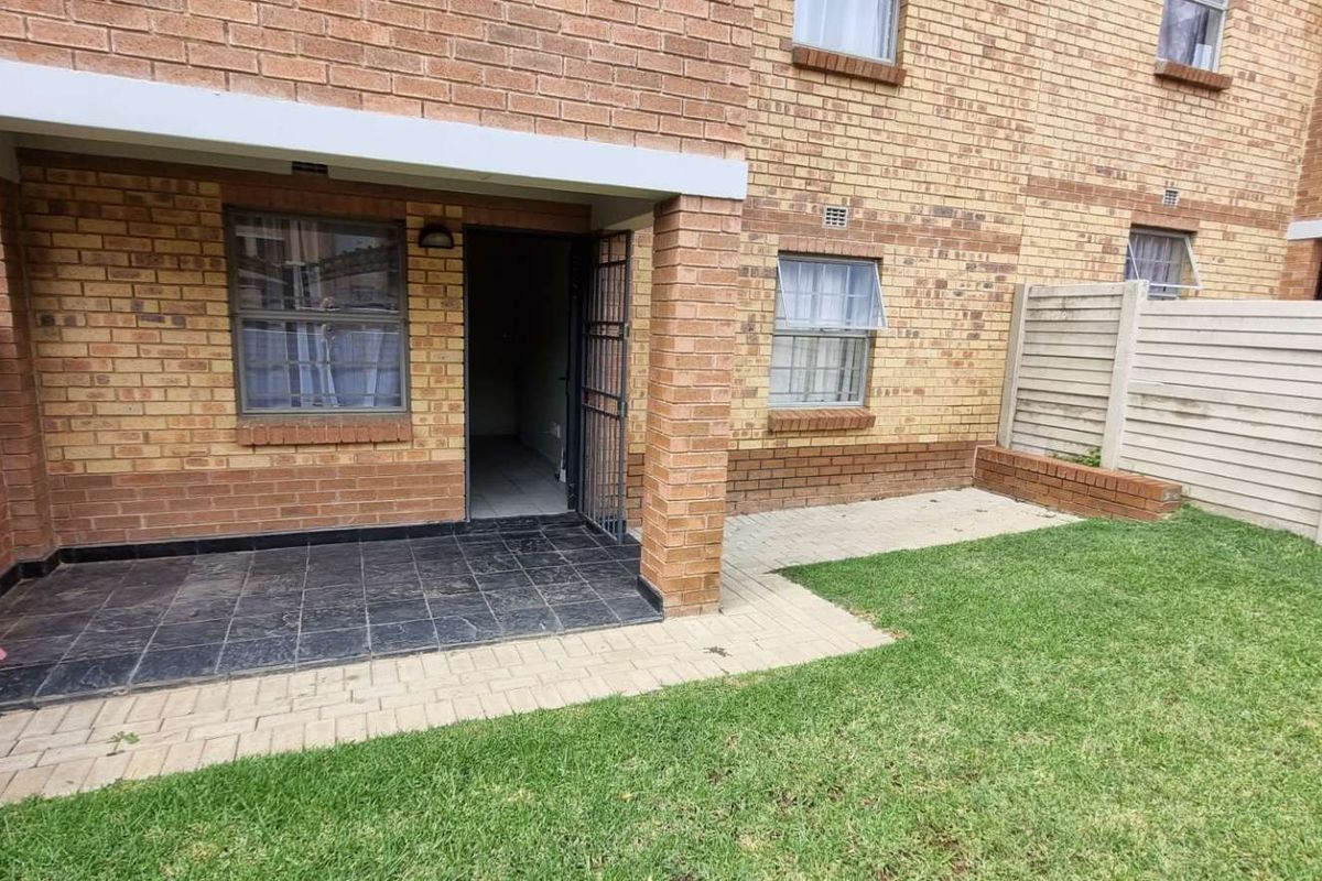 Rear exterior view of the apartment featuring a private tiled patio, paved walkway, and a small enclosed garden area with boundary walling.