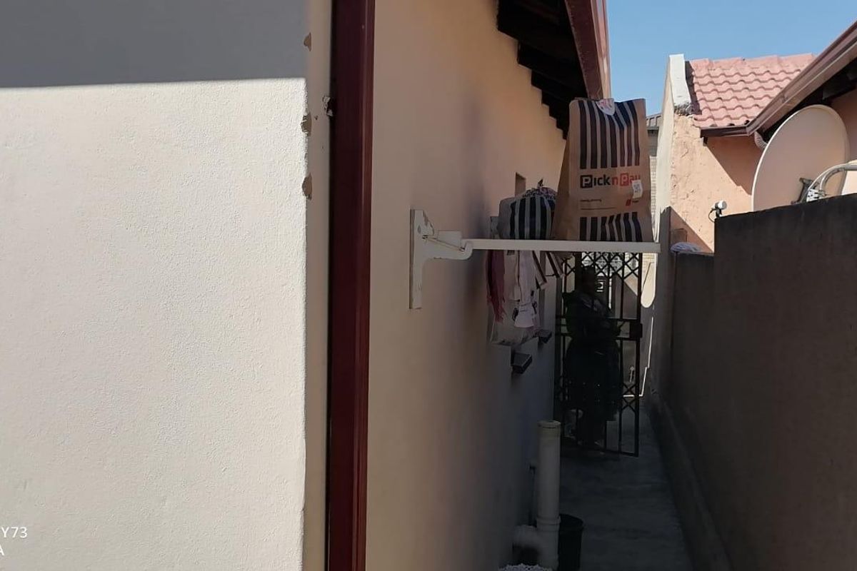 A narrow side passage of the house featuring a wall-mounted drying rack, security gate, and exterior drainage infrastructure.