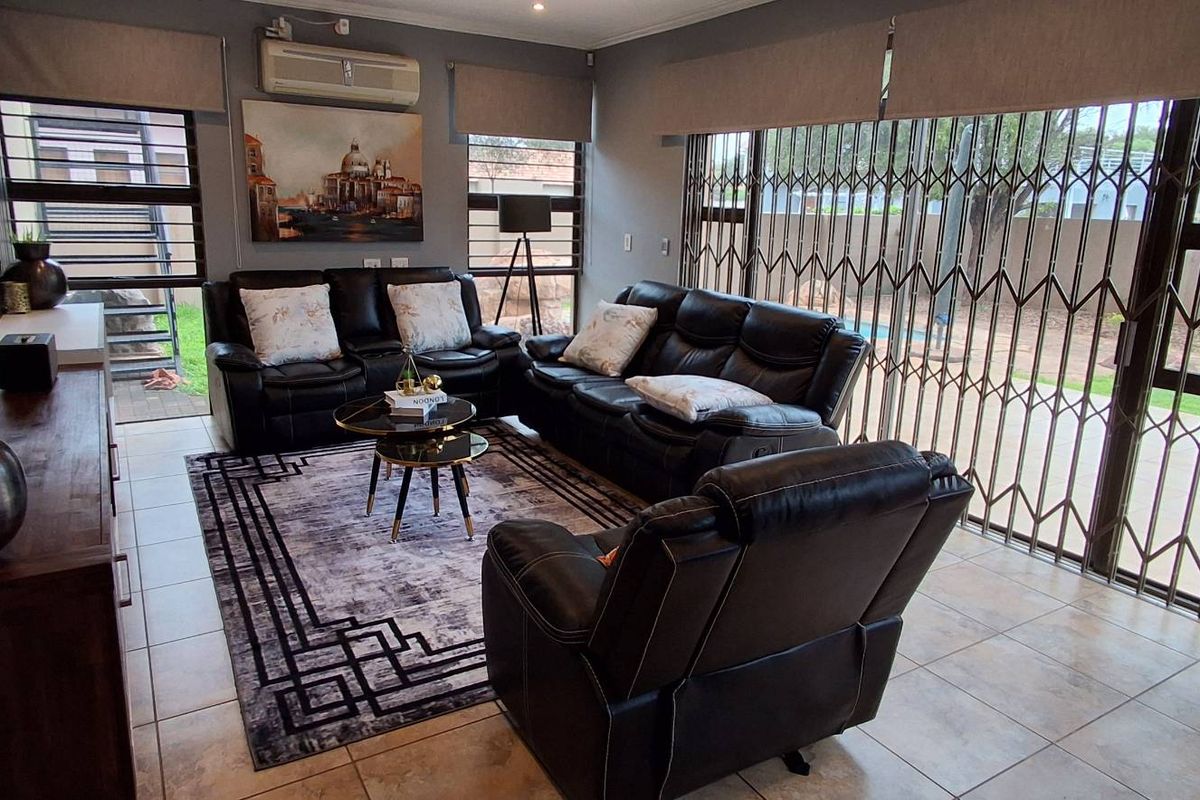 A well-maintained living room featuring tiled flooring, large sliding glass doors with security gates, and a wall-mounted air conditioning unit.