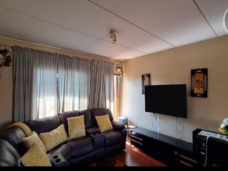 A living room featuring laminate flooring and ceiling panels, currently furnished with a sofa and wall-mounted television.