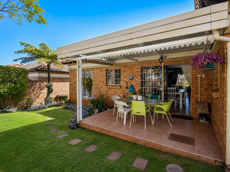 A covered patio area with tiled flooring, featuring direct access to the interior through a sliding glass door and overlooking a private garden.