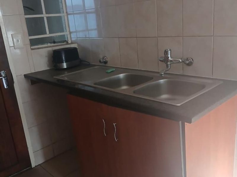 A functional scullery or utility area featuring a double bowl stainless steel sink, tiled splashback, and base cabinetry with laminate countertop.