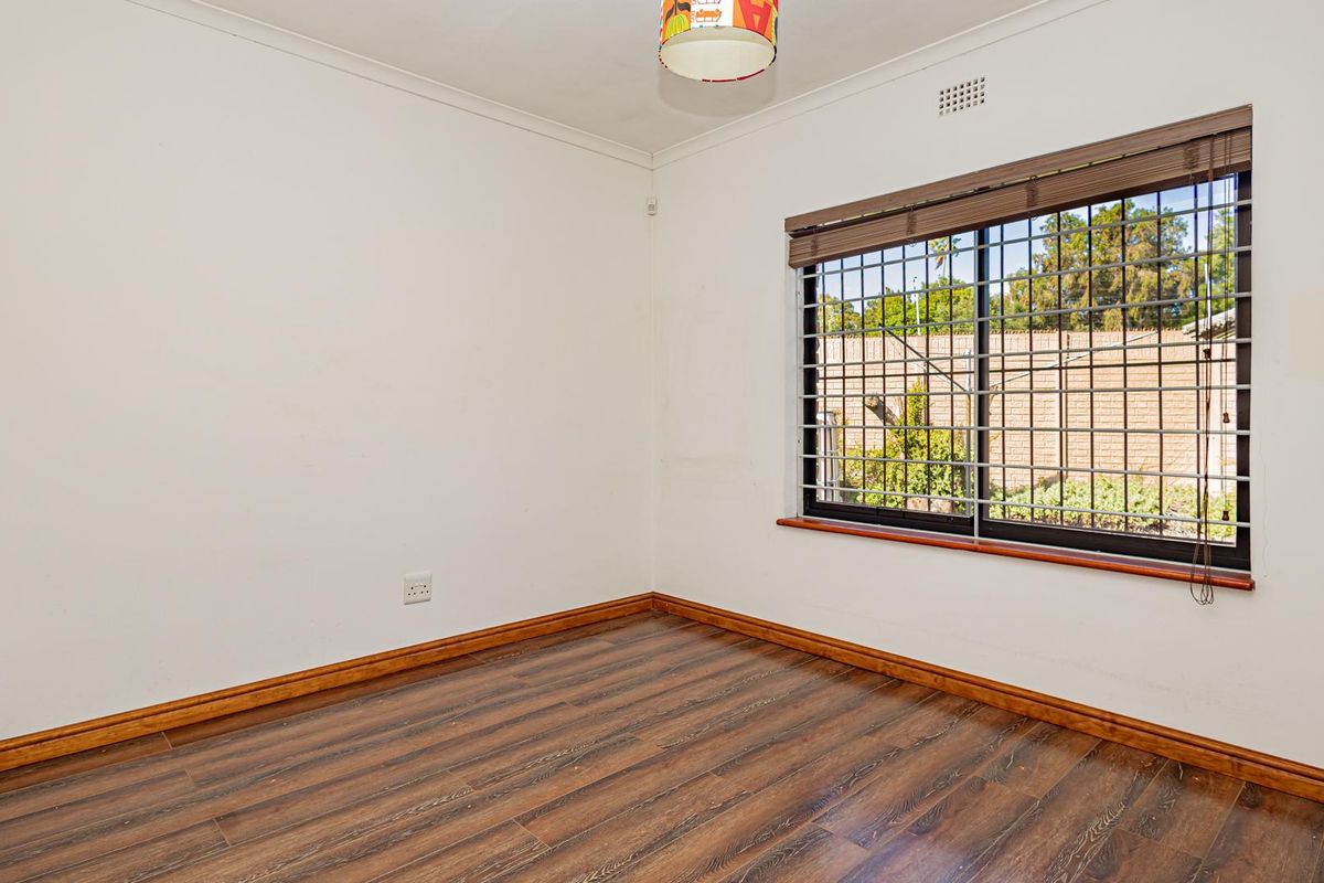 A vacant bedroom featuring laminate flooring, security bars on the window, and neutral wall finishes, offering a clean canvas for personalization.