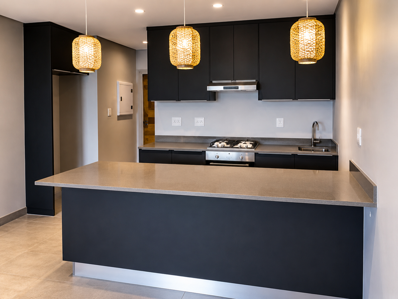 Modern kitchen featuring sleek black cabinetry, stone countertops, a gas hob with extractor fan, and a central island, finished with contemporary lighting.