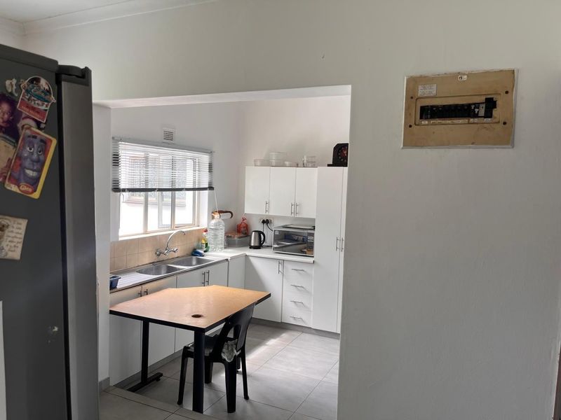 A functional kitchen featuring white cabinetry, a double sink, tiled splashback, and tiled flooring, with an exposed electrical distribution board on the adjacent wall.