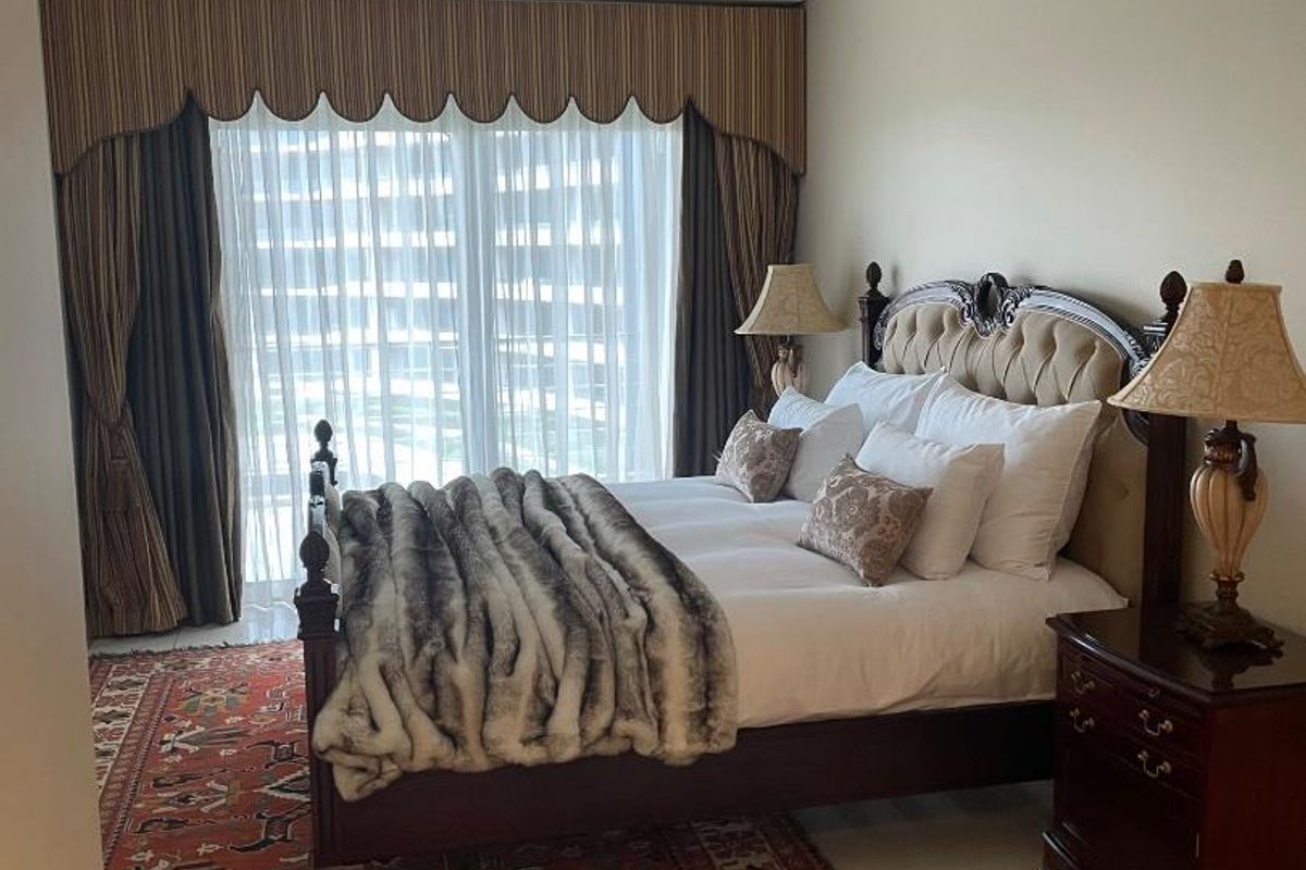 A well-maintained bedroom featuring large windows with floor-to-ceiling curtains, recessed ceiling lighting, and neutral tiled flooring.