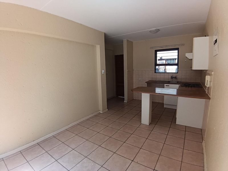 An open-plan kitchen and living area featuring tiled flooring, a breakfast bar, and basic built-in cabinetry with a hob.