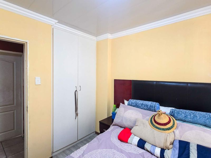 A bedroom featuring built-in wardrobes, crown molding, and laminate flooring, offering a functional space with potential for cosmetic updates.