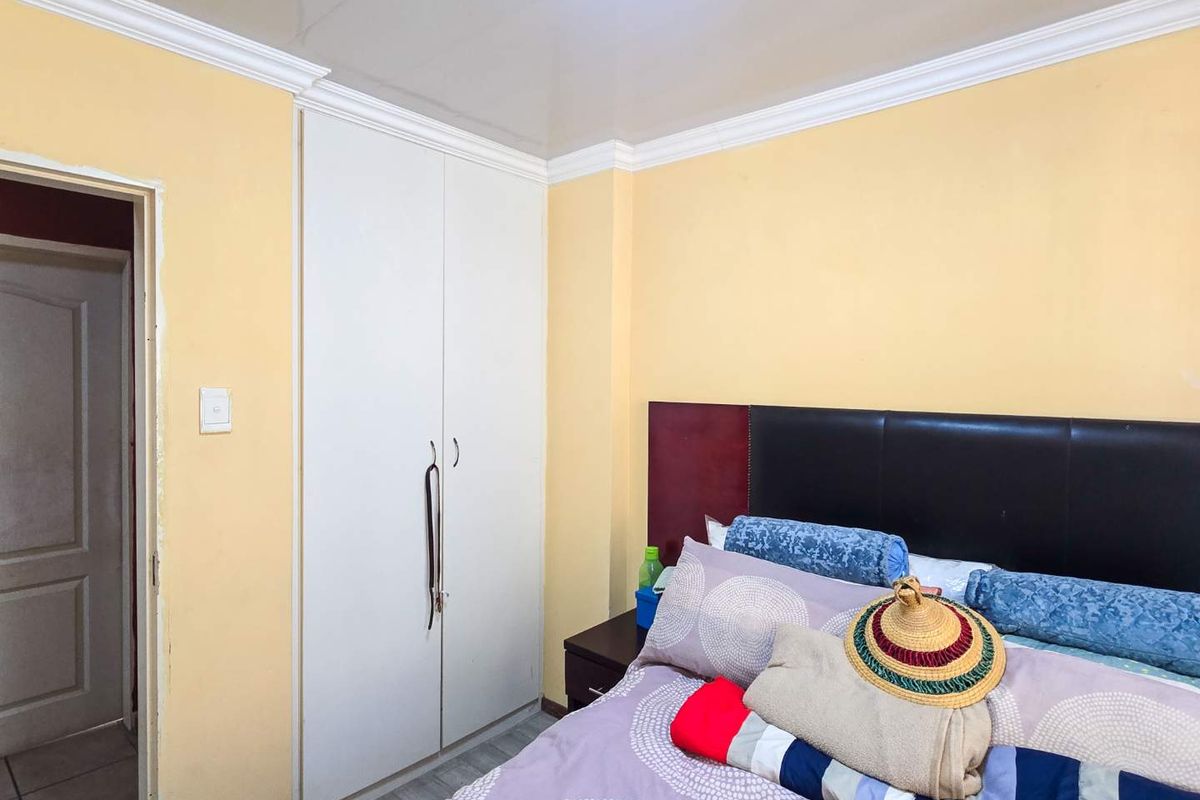 A bedroom featuring built-in wardrobes, crown molding, and laminate flooring, offering a functional space with potential for cosmetic updates.
