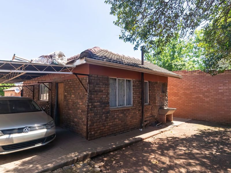Rear view of a face brick house featuring a carport, external wash basin, and surrounding boundary wall.