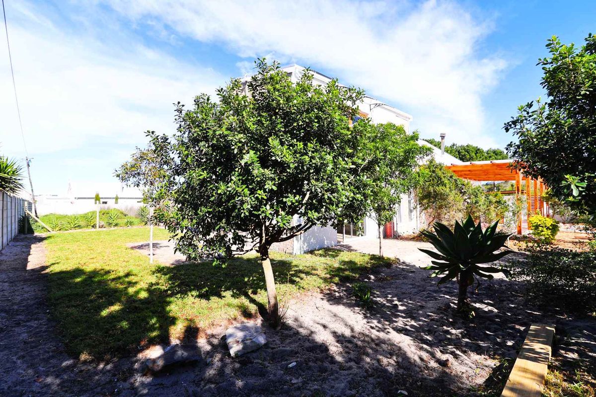 A rear garden view featuring a lawn, mature trees, a paved patio area, and a wooden pergola structure attached to the house.