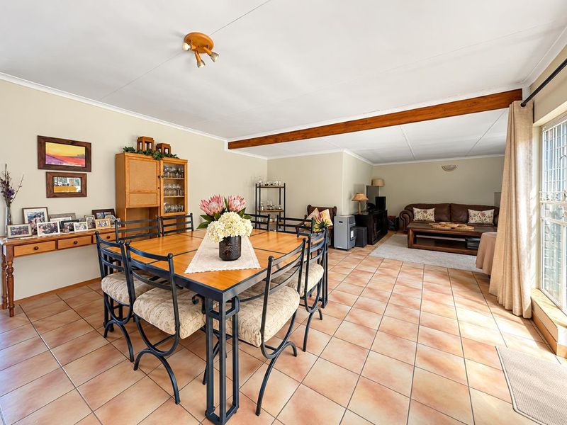 Spacious open-plan living and dining area featuring ceramic floor tiles, an exposed timber ceiling beam, and direct access to the outdoors via sliding doors.