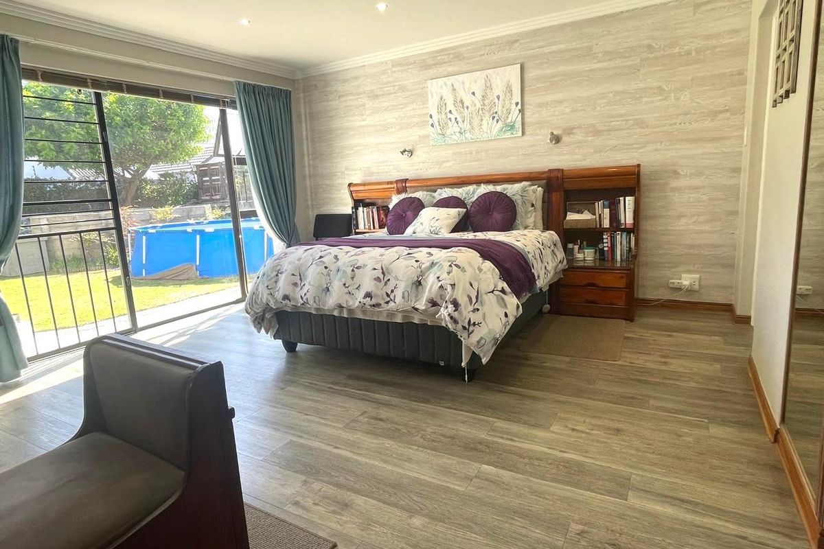 Spacious bedroom featuring wood-look laminate flooring, a feature wall, and large sliding glass doors providing direct access to the garden and pool area.