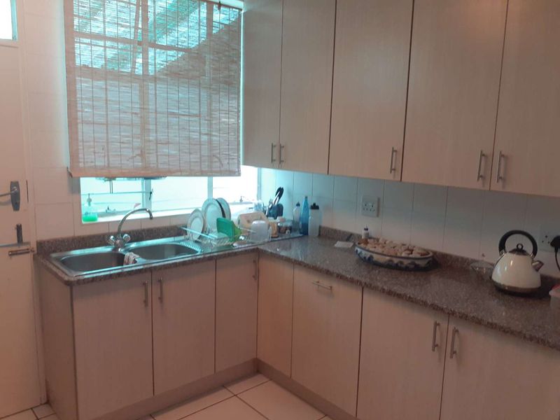 A functional kitchen featuring light-toned laminate cabinetry, granite countertops, and a double basin stainless steel sink with tiled backsplash.