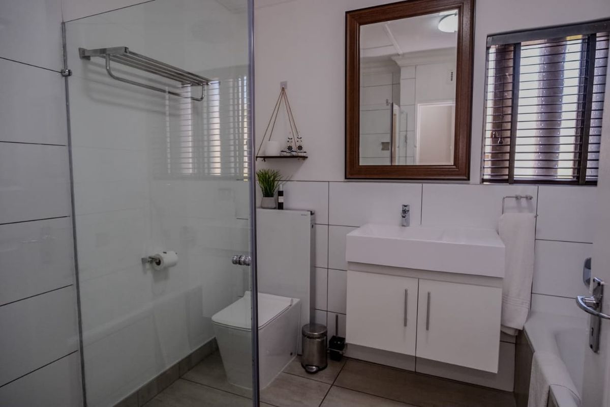 A modern, well-maintained bathroom featuring a glass-enclosed shower, wall-mounted vanity with basin, and clean white tiling throughout.