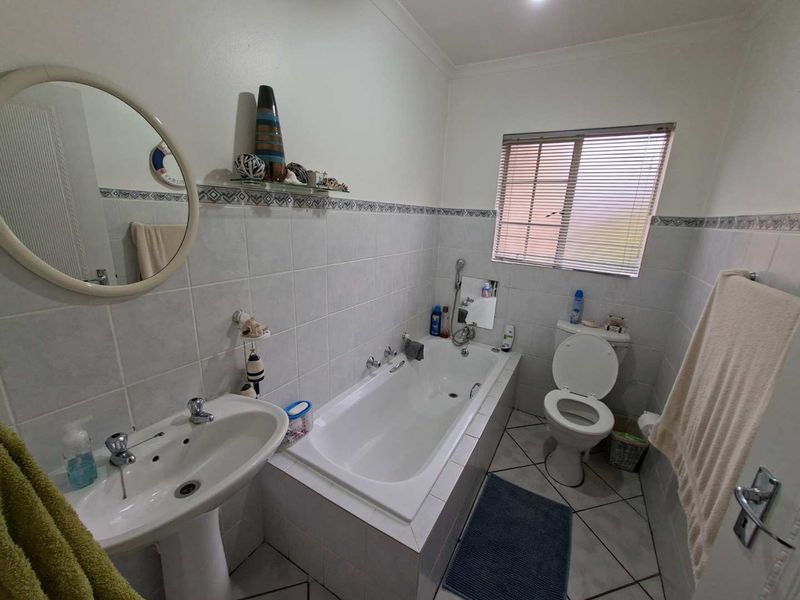 A functional bathroom featuring a pedestal basin, a built-in bathtub, and a toilet, finished with tiled walls and flooring.