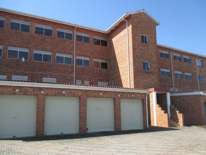 Exterior view of a multi-story brick apartment building featuring a row of garage units and a paved driveway entrance.