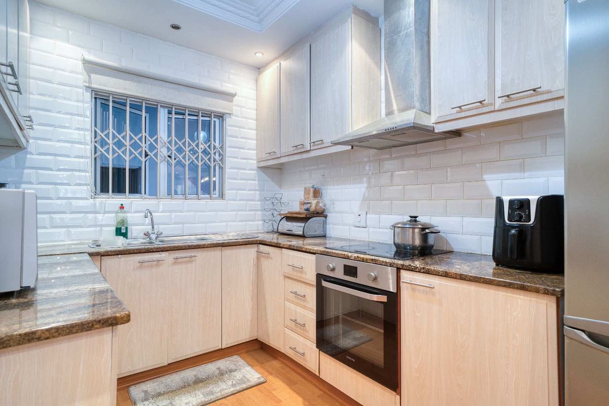A functional kitchen featuring light wood cabinetry, granite countertops, subway tile backsplash, built-in oven, electric hob, and stainless steel extractor fan.