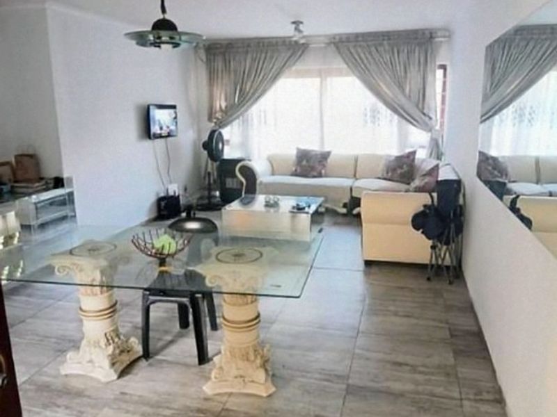 A spacious living area featuring tiled flooring, a large window with curtains, and a wall-mounted mirror, offering a functional layout for relaxation.