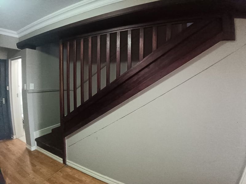 A hallway featuring a wooden staircase with a matching balustrade, crown molding, and laminate flooring.