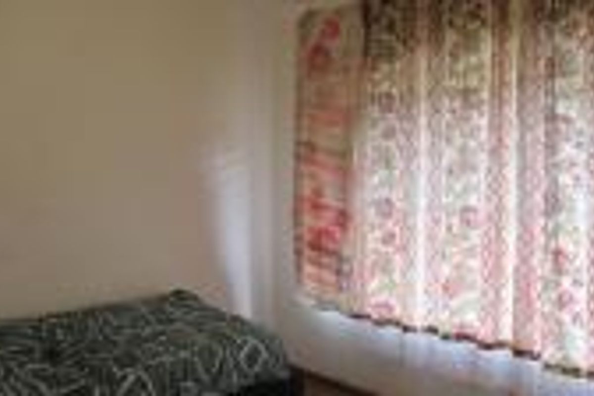 A simple bedroom featuring a large window with patterned curtains and neutral wall finishes.