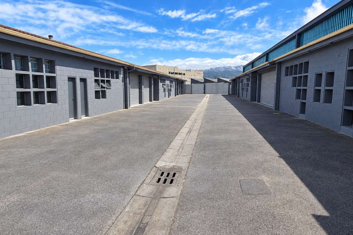A well-maintained industrial complex exterior featuring asphalt driveway, concrete block walls, and multiple roller shutter access points.