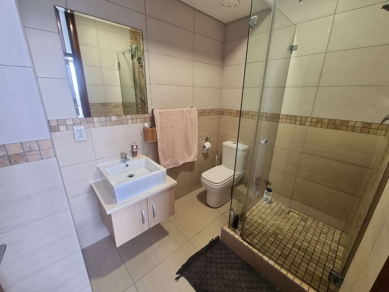 A modern bathroom featuring a wall-mounted vanity with a vessel sink, a glass-enclosed shower with mosaic tiling, and neutral ceramic wall tiles.