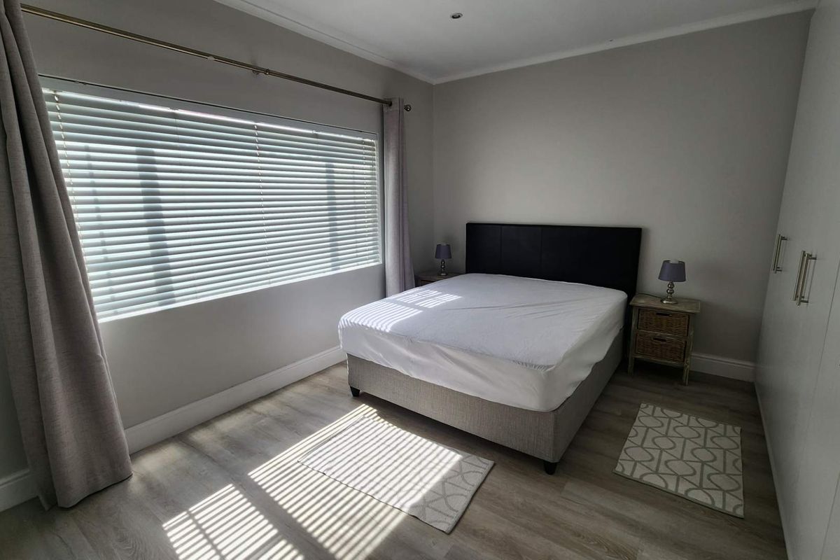 A well-maintained bedroom featuring light laminate flooring, built-in cupboards, and venetian blinds, offering a clean and neutral living space.