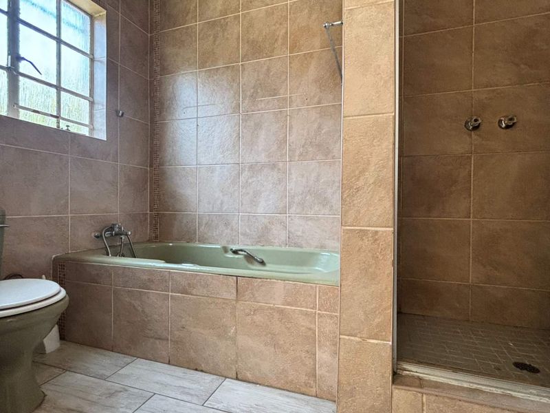 A dated bathroom featuring a built-in bathtub, separate shower enclosure, and toilet with neutral wall and floor tiling.