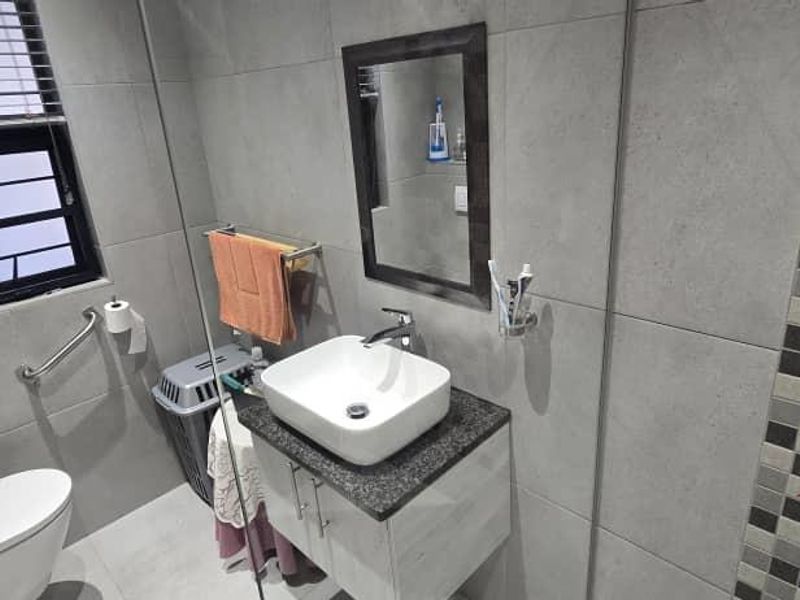 Modern bathroom featuring grey tiled walls, a vessel sink vanity, and a wall-mounted grab bar near the toilet.