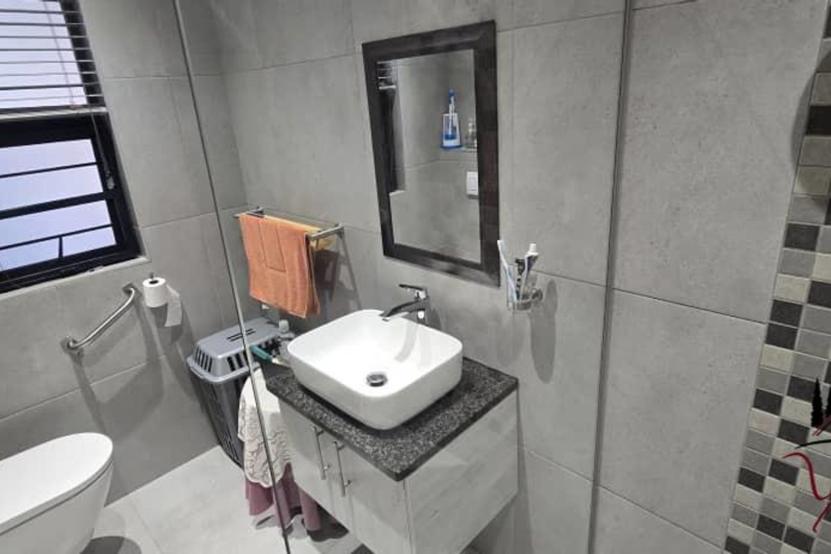 Modern bathroom featuring grey tiled walls, a vessel sink vanity, and a wall-mounted grab bar near the toilet.