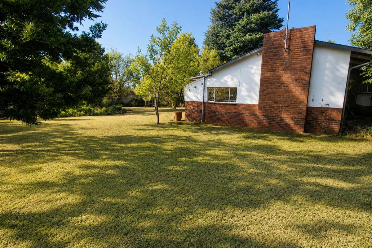 A view of the rear garden featuring a large lawn, mature trees, and the side elevation of the house with a prominent brick chimney.