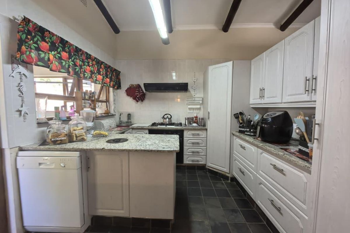 A functional kitchen featuring granite countertops, white cabinetry, exposed ceiling beams, and a gas hob with an extractor fan.