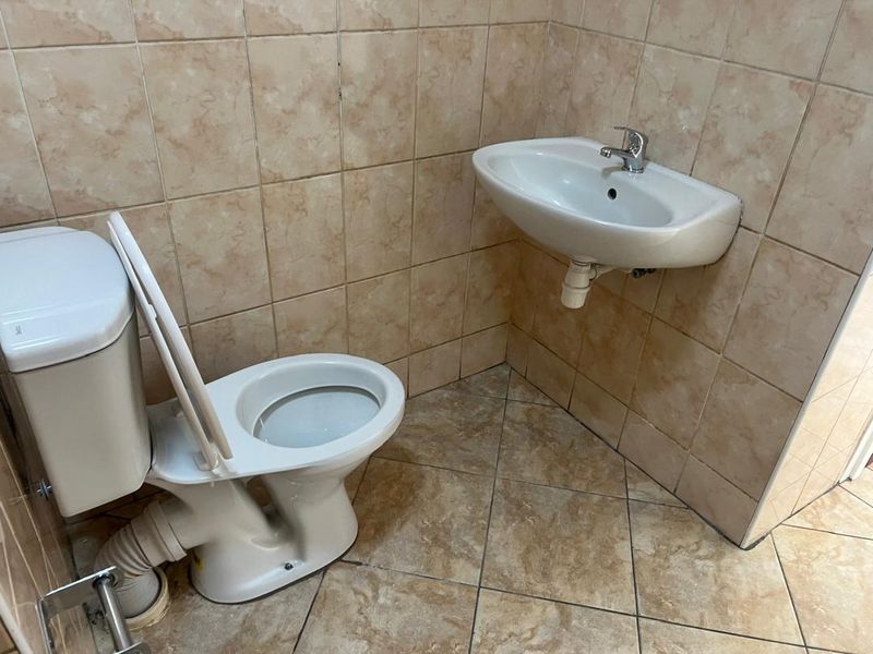 A functional bathroom featuring a wall-mounted basin and standard ceramic toilet with neutral wall and floor tiling.