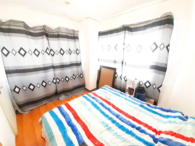 A bedroom featuring laminate flooring and large windows covered by patterned curtains.