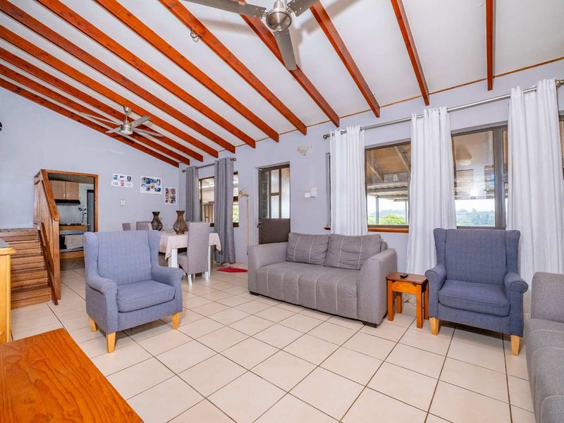 Spacious open-plan living and dining area featuring exposed timber ceiling beams, tiled flooring, and direct access to a staircase.