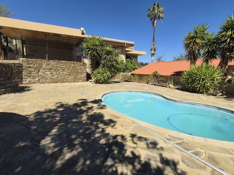 Outdoor pool area featuring a stone-paved patio, a kidney-shaped swimming pool, and a covered patio space with stone retaining walls.