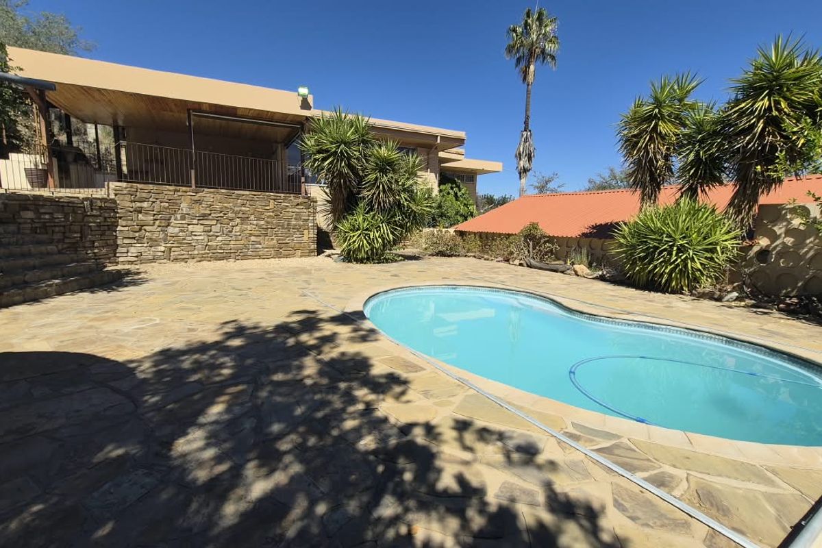 Outdoor pool area featuring a stone-paved patio, a kidney-shaped swimming pool, and a covered patio space with stone retaining walls.
