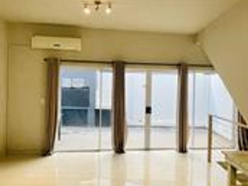 An open-plan living area featuring tiled flooring, a wall-mounted air conditioning unit, and large sliding glass doors leading to an outdoor space.