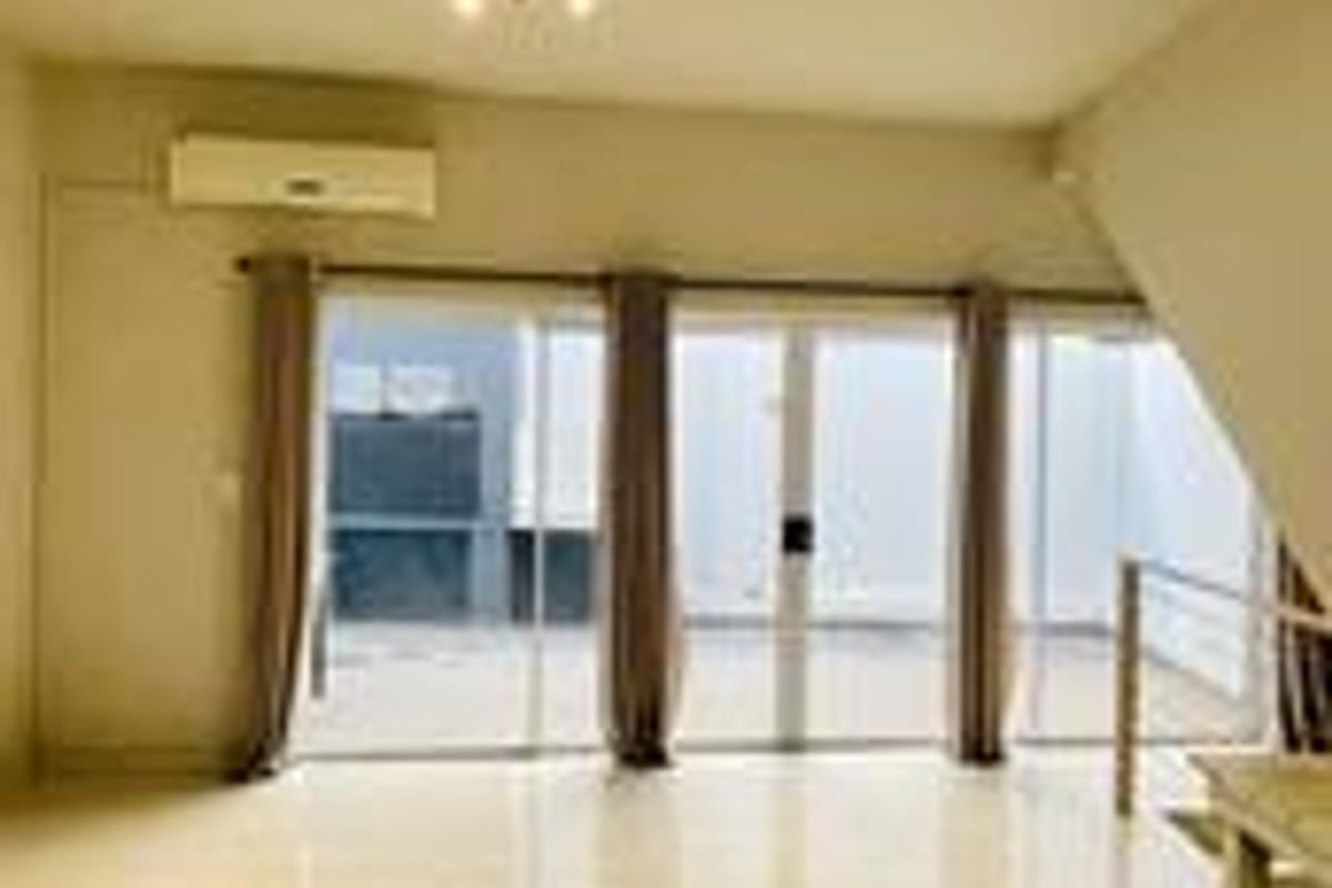 An open-plan living area featuring tiled flooring, a wall-mounted air conditioning unit, and large sliding glass doors leading to an outdoor space.