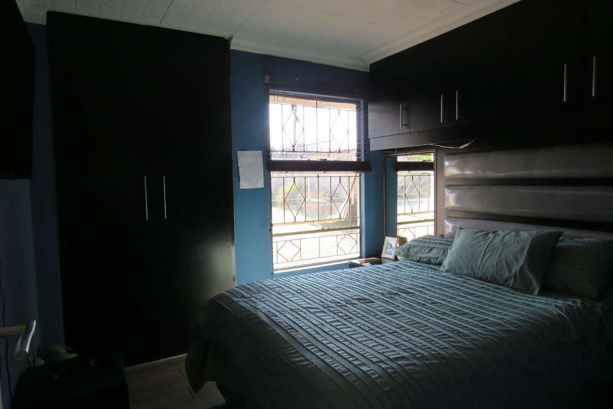 A bedroom featuring built-in dark cabinetry, overhead storage units, and security bars on the windows.