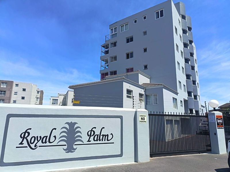 Front exterior view of the Royal Palm apartment complex, featuring a secure gated entrance, boundary wall, and modern multi-story building facade.
