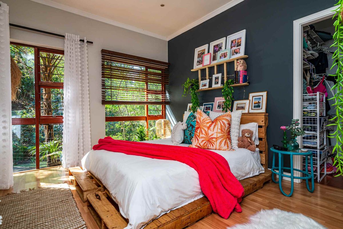 A bright bedroom featuring wooden flooring, large windows with timber blinds, and an integrated walk-in closet space.