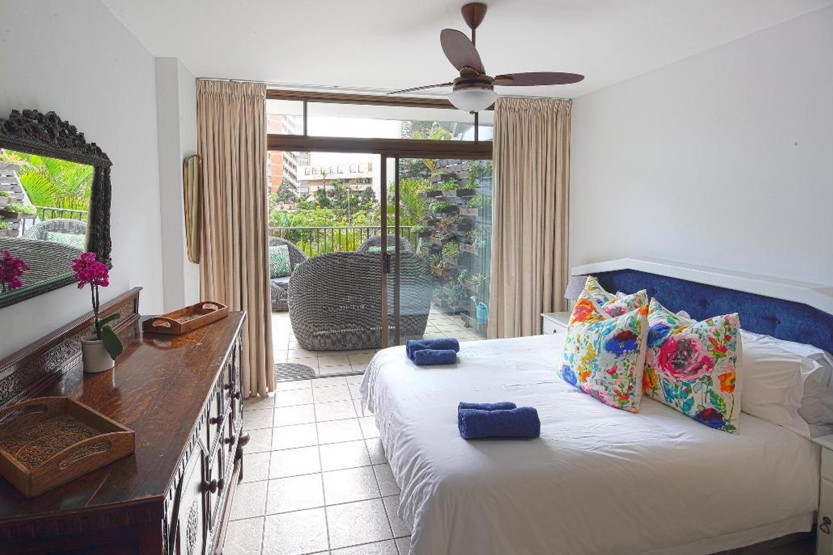 A bright bedroom featuring tiled flooring, a ceiling fan, and large sliding glass doors that open onto a private balcony.